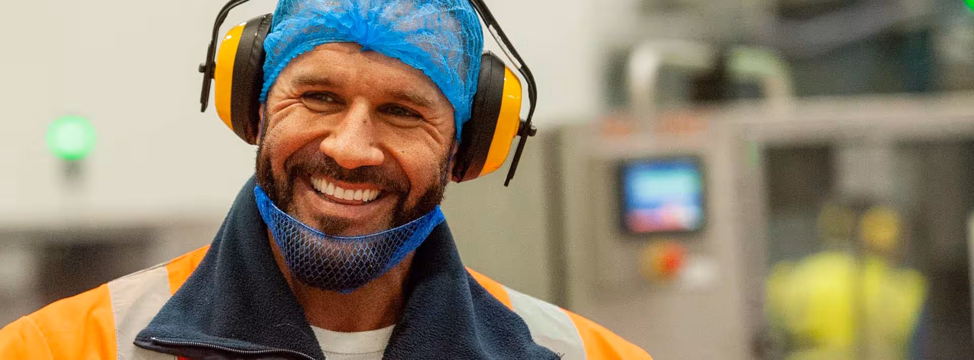 Man smiling to camera wearing hair net and ear defenders in a warehouse